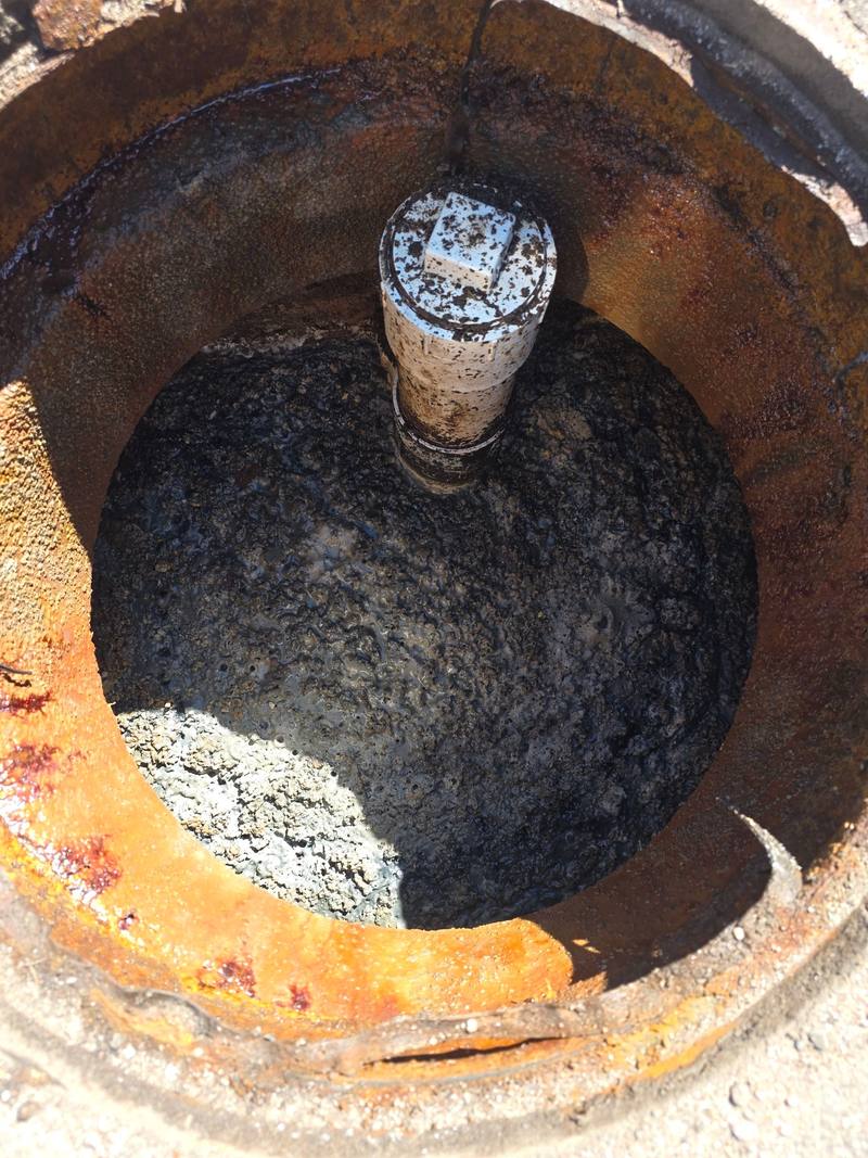 Round interceptor opening with a capped pipe standing in a thick layer of grease and sludge
