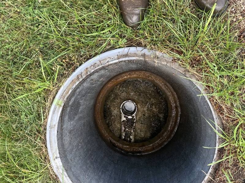 Looking down into an open septic cleanout pipe, with a crew member's boots at the edge